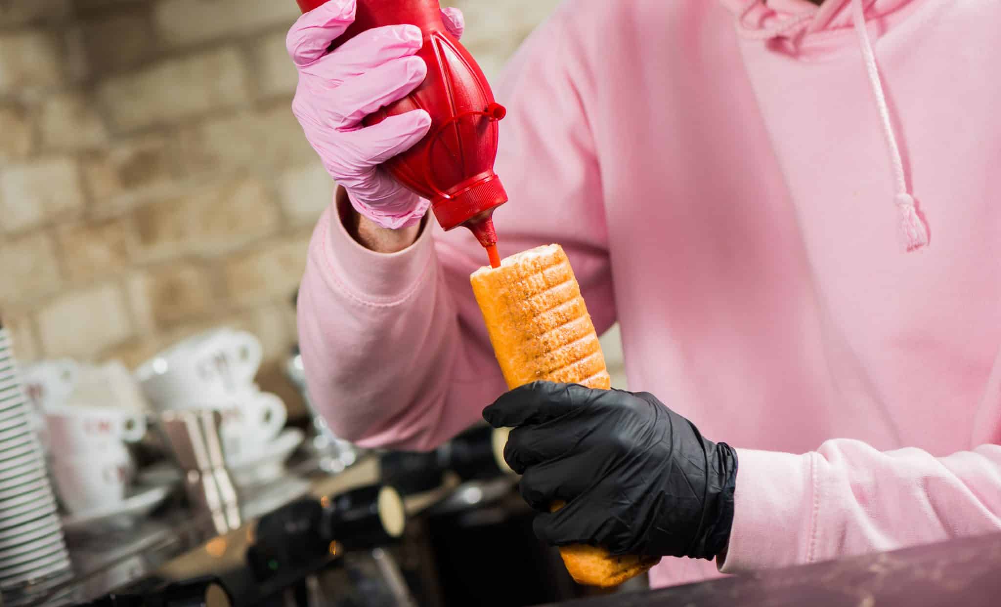 bartender adding ketchup sauce in french hot dog with grill sausage