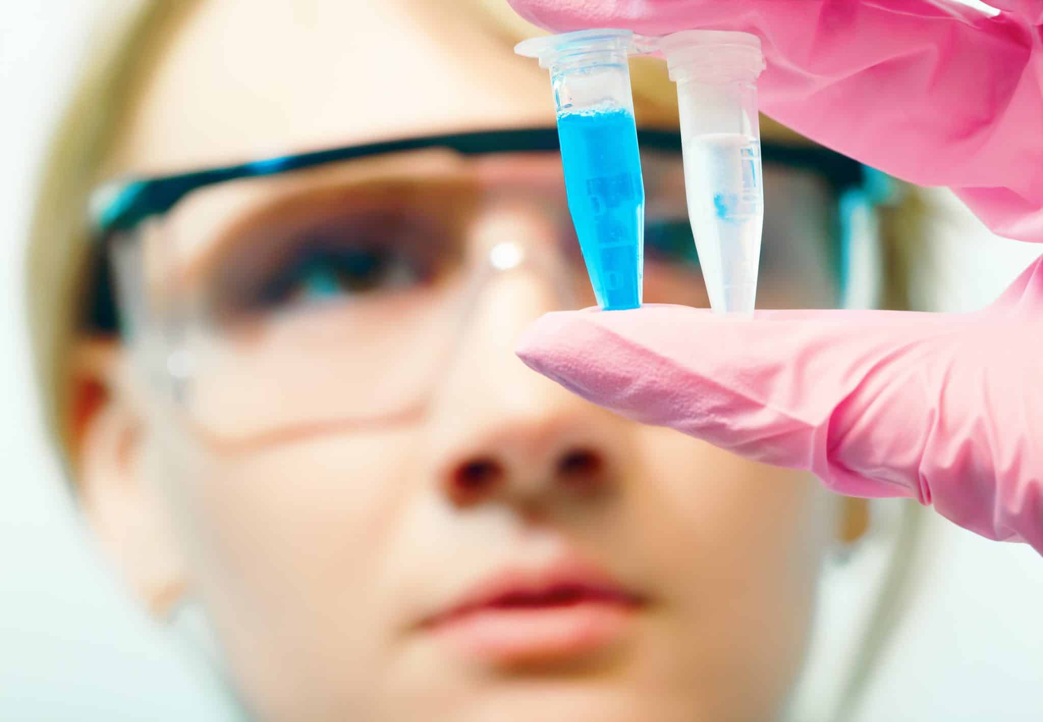 low focus portrait of young woman scientist analyzing two test tubes, face on background